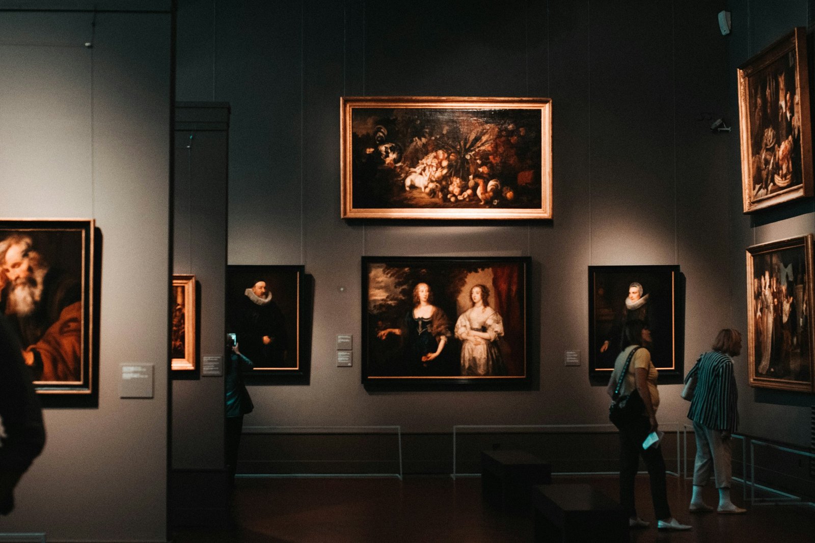 Visitors viewing paintings in a dim gallery